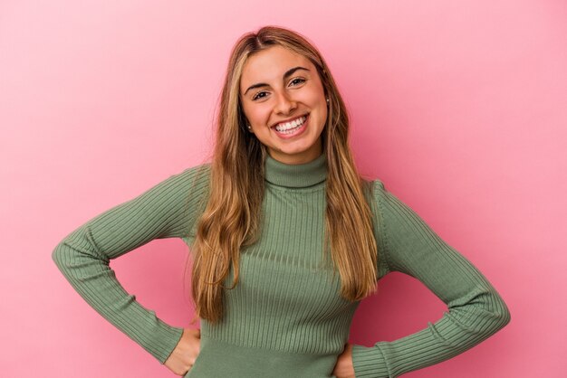 Giovane donna caucasica bionda isolata sul muro rosa fiducioso mantenendo le mani sui fianchi