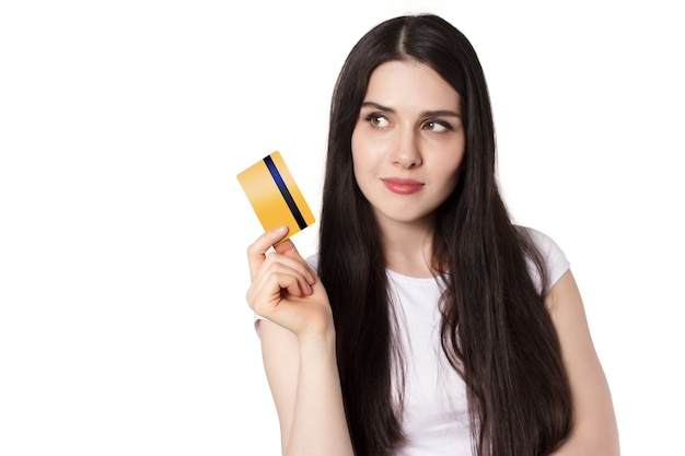 Giovane donna caucasica bruna in maglietta bianca che dimostra la sua carta di credito bancaria d'oro per mock up