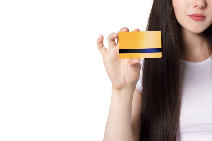 Giovane donna caucasica bruna in maglietta bianca che tiene in mano una carta di credito bancaria per mock up