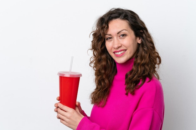 Giovane donna caucasica che beve soda isolata su sfondo bianco sorridente molto