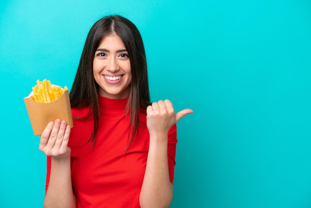 Giovane donna caucasica che cattura le patatine fritte isolate su sfondo blu che indica il lato per presentare un prodotto