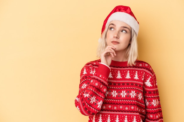 Giovane donna caucasica che celebra il Natale isolato su sfondo giallo guardando di traverso con espressione dubbiosa e scettica.