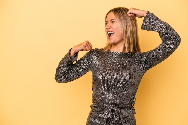 Giovane donna caucasica che celebra il nuovo anno isolata su fondo giallo che alza il pugno dopo una vittoria, concetto del vincitore.