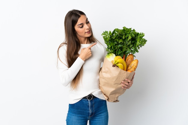 Giovane donna caucasica che compra del cibo isolato sul muro bianco che punta di lato per presentare un prodotto