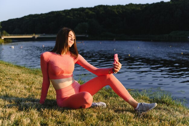 Giovane donna caucasica che fa esercizio di allenamento attivo su un tappetino da yoga vicino al fiume in estate. Concetto di stile di vita sano