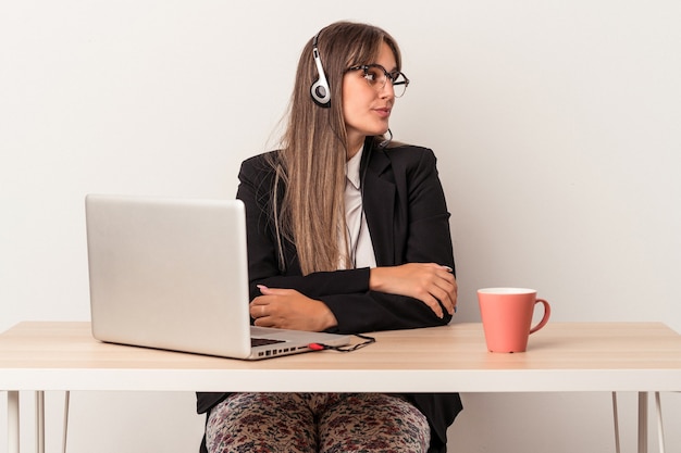 Giovane donna caucasica che fa il telelavoro isolato su sfondo bianco guardando a sinistra, posa laterale.