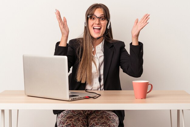 Giovane donna caucasica che fa il telelavoro isolato su sfondo bianco ricevendo una piacevole sorpresa, eccitata e alzando le mani.