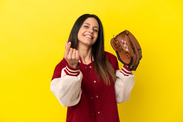 Giovane donna caucasica che gioca a baseball isolata su fondo giallo che fa il gesto dei soldi