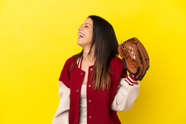 Giovane donna caucasica che gioca a baseball isolata su sfondo giallo ridendo in posizione laterale