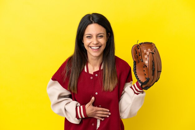 Giovane donna caucasica che gioca a baseball isolata su sfondo giallo sorridendo molto