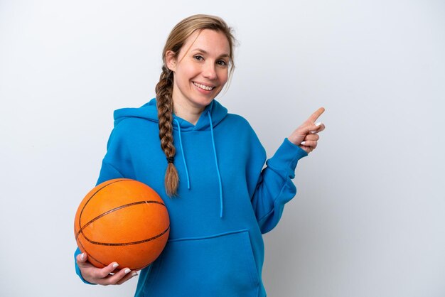 Giovane donna caucasica che gioca a basket isolata su sfondo bianco che punta il dito di lato