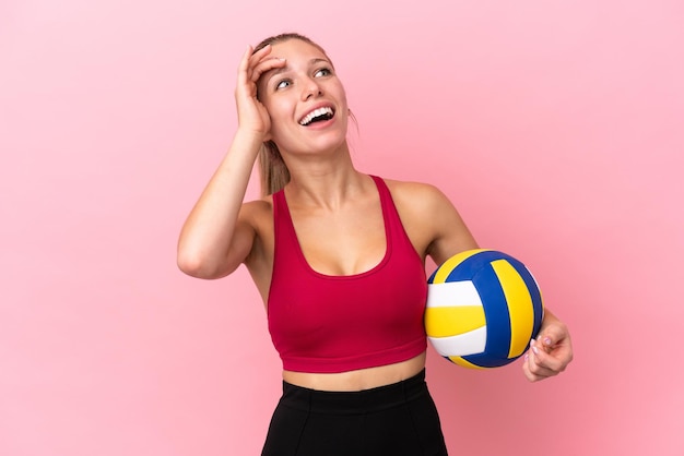 Giovane donna caucasica che gioca a pallavolo isolata su sfondo rosa che sorride molto