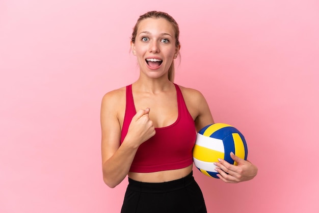 Giovane donna caucasica che gioca a pallavolo isolata su sfondo rosa con espressione facciale a sorpresa