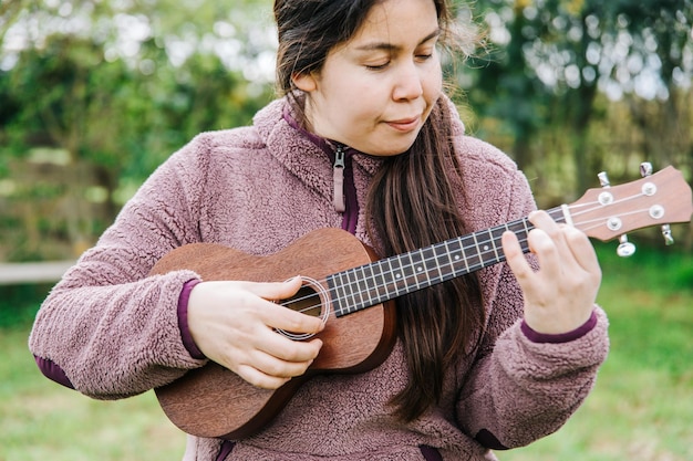 Giovane donna caucasica che gioca ukelele in piedi sull'erba.