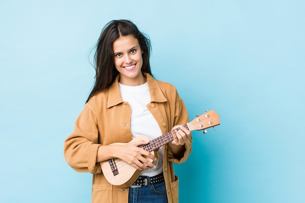 Giovane donna caucasica che gioca ukelele isolato sull'azzurro