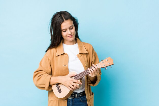 Giovane donna caucasica che gioca ukelele su una parete blu