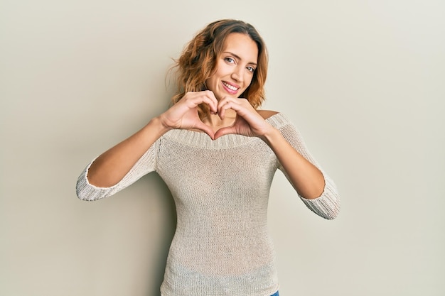 Giovane donna caucasica che indossa abiti casual sorridenti innamorati che fanno la forma del simbolo del cuore con le mani. concetto romantico.