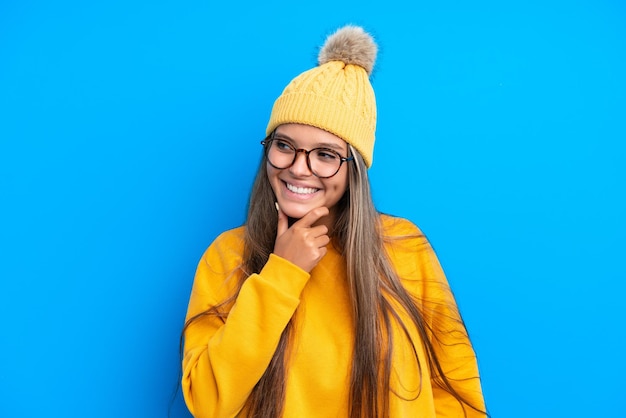 Giovane donna caucasica che indossa abiti invernali isolati su sfondo blu guardando di lato e sorridente