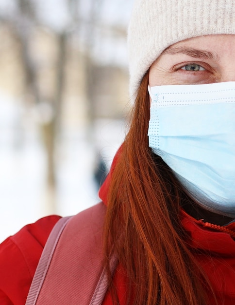 Giovane donna caucasica che indossa la maschera medica guardando la telecamera in strada della città. Sicurezza in luoghi pubblici durante l'epidemia di coronavirus.