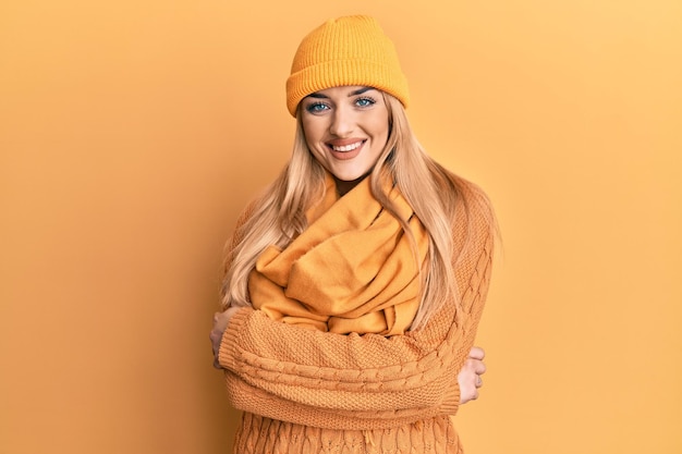Giovane donna caucasica che indossa maglione invernale di lana e berretto faccia felice sorridente con le braccia incrociate guardando la telecamera. persona positiva.