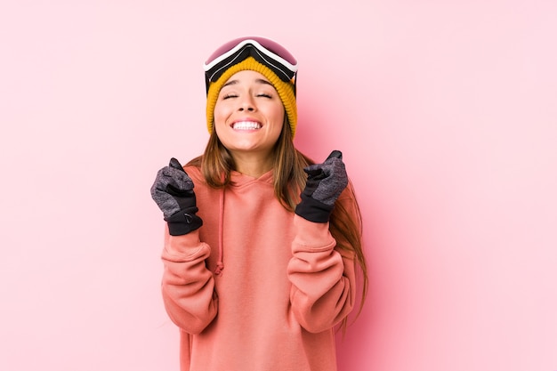 Giovane donna caucasica che indossa un abbigliamento da sci isolato alzando il pugno, sentendosi felice e di successo. Concetto di vittoria.