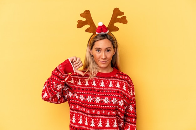 Giovane donna caucasica che indossa un cappello da renna di natale isolato su sfondo beige che mostra un gesto di antipatia, pollice verso. Concetto di disaccordo.