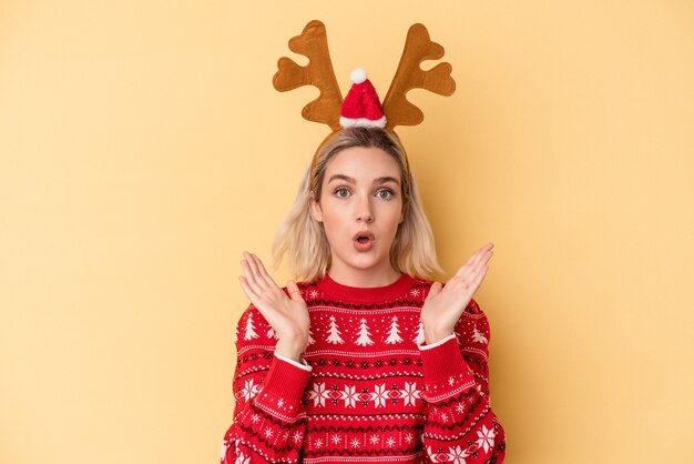 Giovane donna caucasica che indossa un cappello di renne di Natale isolato su sfondo giallo sorpreso e scioccato.