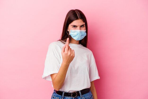 Giovane donna caucasica che indossa una maschera per virus isolato sul muro rosa che punta il dito contro di te