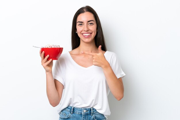 Giovane donna caucasica che mangia latte per la colazione isolato su sfondo bianco e indicandolo