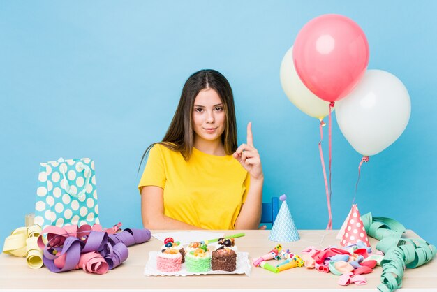 Giovane donna caucasica che organizza un compleanno che mostra numero uno con il dito.