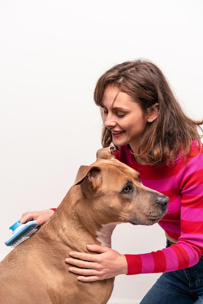 Giovane donna caucasica che pettina il suo cane isolato su priorità bassa bianca