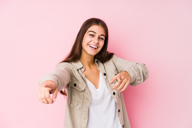 Giovane donna caucasica che posa nei sorrisi allegri di una parete rosa che indica la parte anteriore.