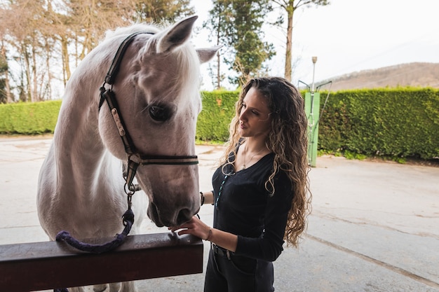 Giovane donna caucasica che prepara un cavallo bianco per un giro