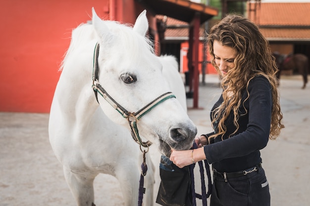 Giovane donna caucasica che prepara un cavallo bianco per un giro