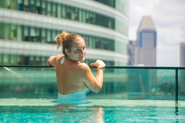 Giovane donna caucasica che si rilassa in una piscina sul tetto di un grattacielo in una metropoli sotto il sole