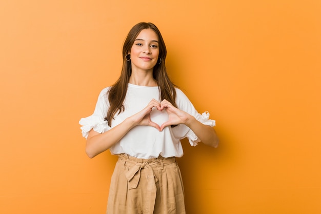 Giovane donna caucasica che sorride e che mostra una forma del cuore con le mani.