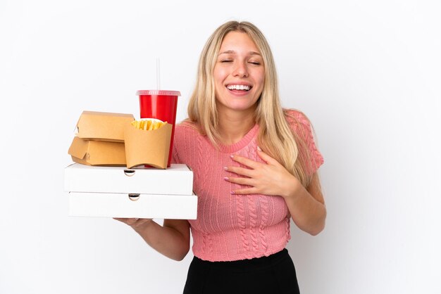 Giovane donna caucasica che tiene cibo grasso isolato su sfondo blu sorridente molto