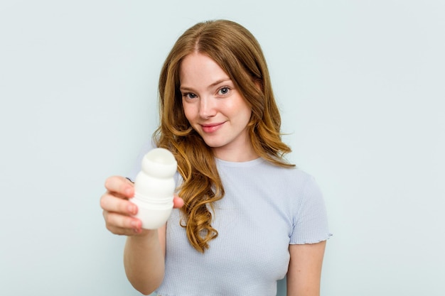 Giovane donna caucasica che tiene deodorante isolato su sfondo blu