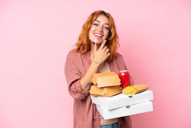 Giovane donna caucasica che tiene fast food isolato su sfondo rosa felice e sorridente