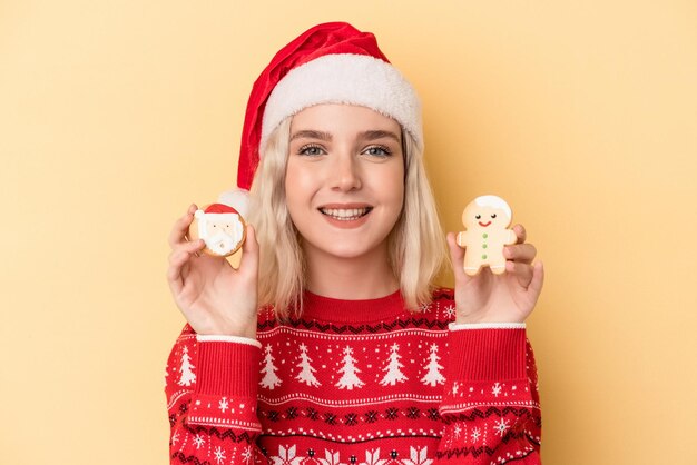 Giovane donna caucasica che tiene i biscotti di Natale isolati su sfondo giallo