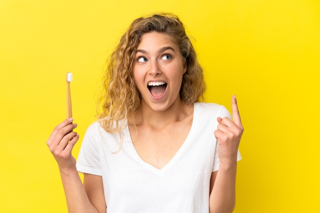 Giovane donna caucasica che tiene in mano un lavarsi i denti isolato su sfondo giallo pensando a un'idea che punta il dito