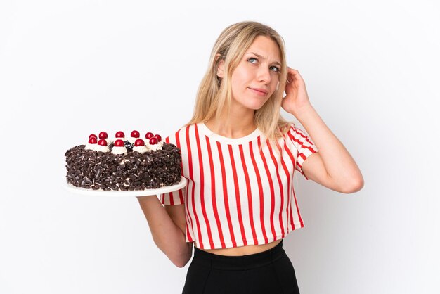 Giovane donna caucasica che tiene la torta di compleanno isolata su fondo bianco che ha dubbi