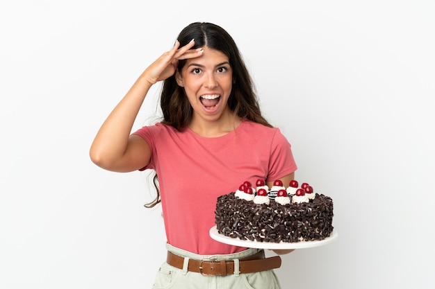 Giovane donna caucasica che tiene la torta di compleanno isolata su fondo bianco con l'espressione di sorpresa