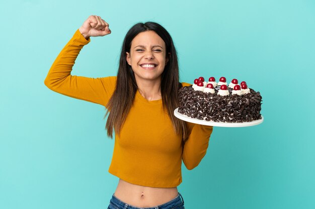 Giovane donna caucasica che tiene la torta di compleanno isolata su fondo blu che fa un gesto forte