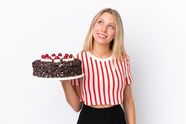 Giovane donna caucasica che tiene la torta di compleanno isolata su sfondo bianco pensando a un'idea mentre alza lo sguardo