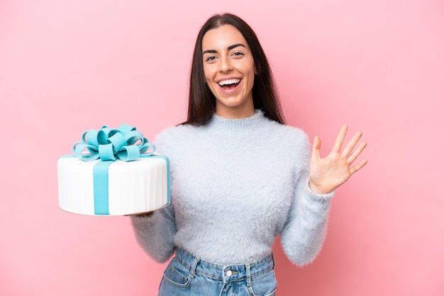 Giovane donna caucasica che tiene la torta di compleanno isolata su sfondo rosa contando cinque con le dita