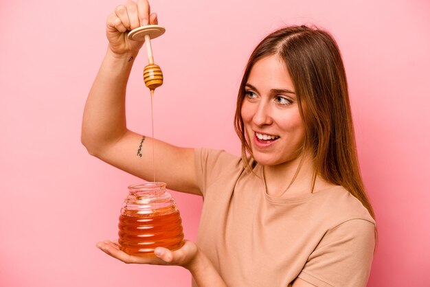 Giovane donna caucasica che tiene miele isolato su sfondo rosa