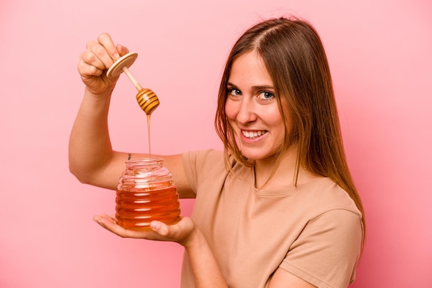 Giovane donna caucasica che tiene miele isolato su sfondo rosa