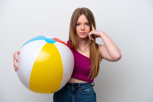 Giovane donna caucasica che tiene pallone da spiaggia isolato su sfondo bianco pensando un'idea