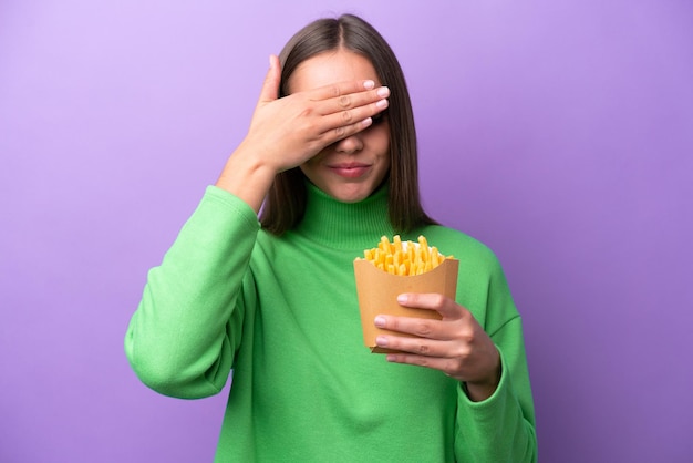 Giovane donna caucasica che tiene patatine fritte su sfondo viola che copre gli occhi con le mani Non voglio vedere qualcosa